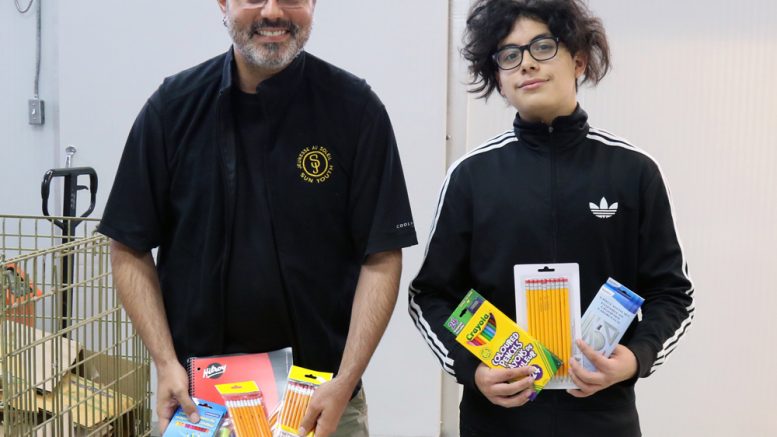 The Senior Times’ volunteer Prospero Monroy Demesa (right) delivers school supplies to Sun Youth’s Nicolas Carpentier August 29 to fulfill the needs of children on the waiting list.